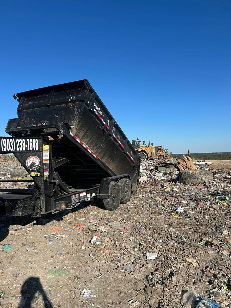 Black dump truck with raised bed unloading debris at a landfill or construction waste site under clear blue sky